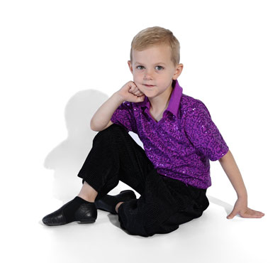 A young boy in a purple patterned dance shirt and black pants sitting on the floor in a relaxed pose against a white background.